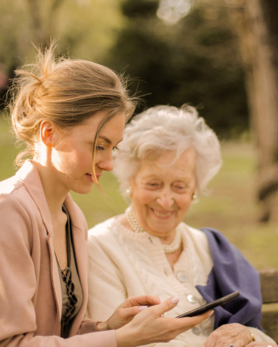 Une dame de compagnie Maison Helya en promenade avec sa cliente lui montre des photos sur son téléphone